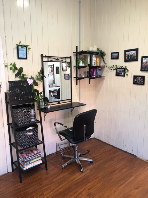 A styling station with mirror, chair, shelves and framed photos on the timber wall