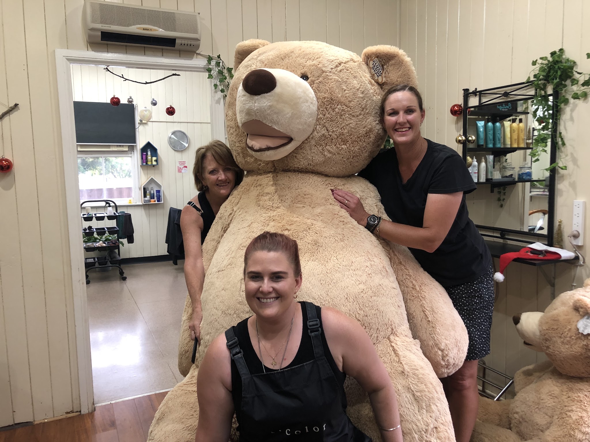 Three of the Beauty and the Barber team smiling with a giant teddy bear inside the salon at Christmas